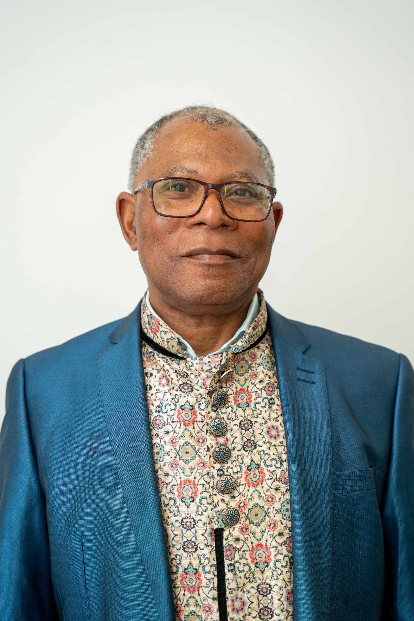 Headshot of Councillor Anyanwu wearing glasses, a blue blazer and a patterned shirt