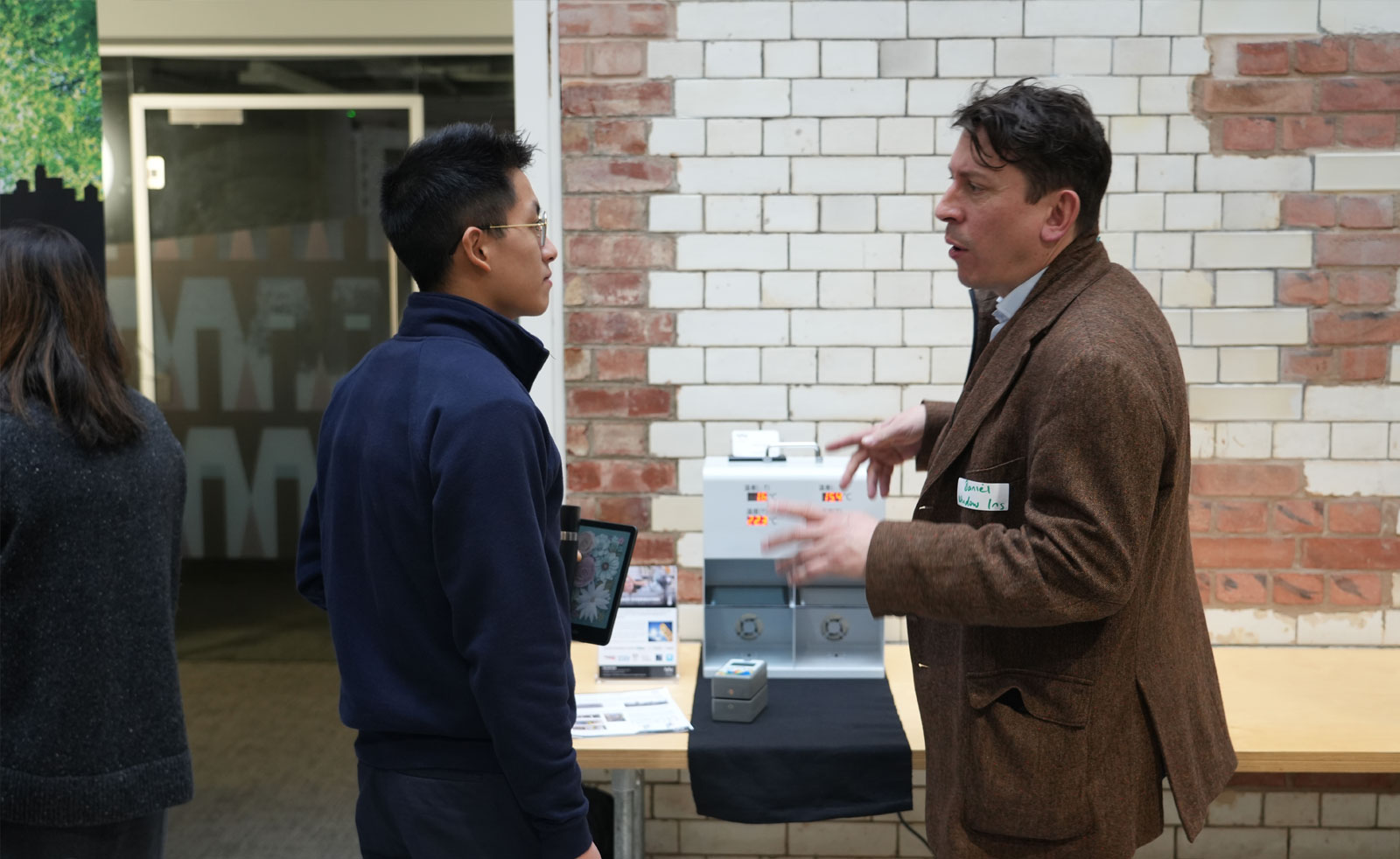Two climate tech product innovators stand speaking in front of the product exhibition table.