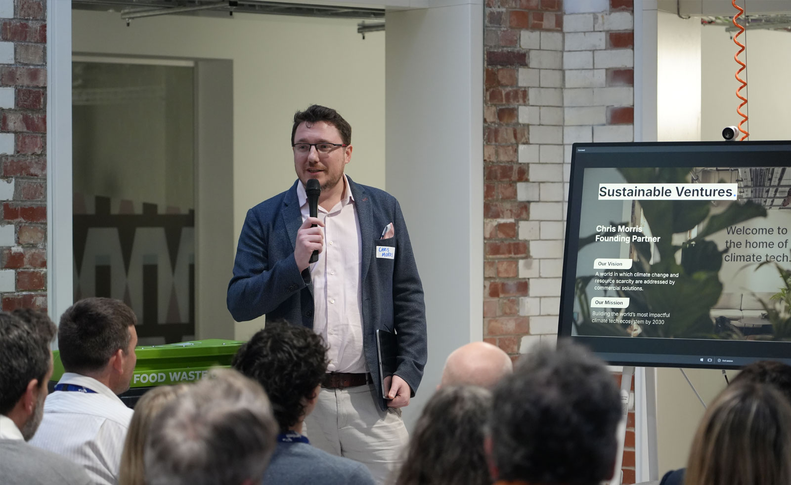 A speaker stands in front of an audience giving an introduction speech as part of the Pitch Day event.