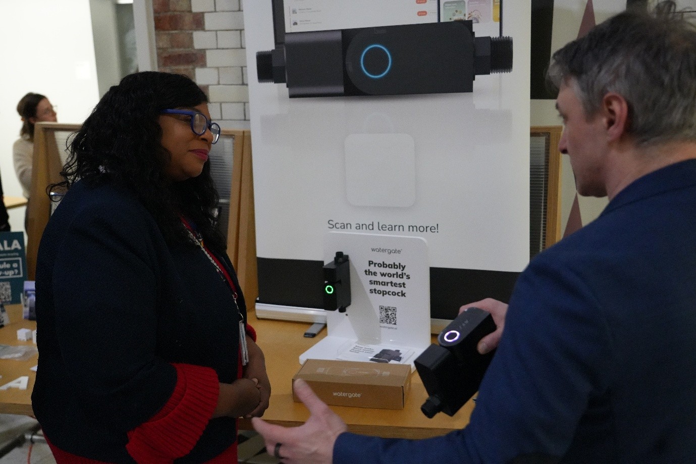 The Cabinet Member for Economic Inclusion stands talking to a climate tech product innovator in front of an exhibition stand of their product.