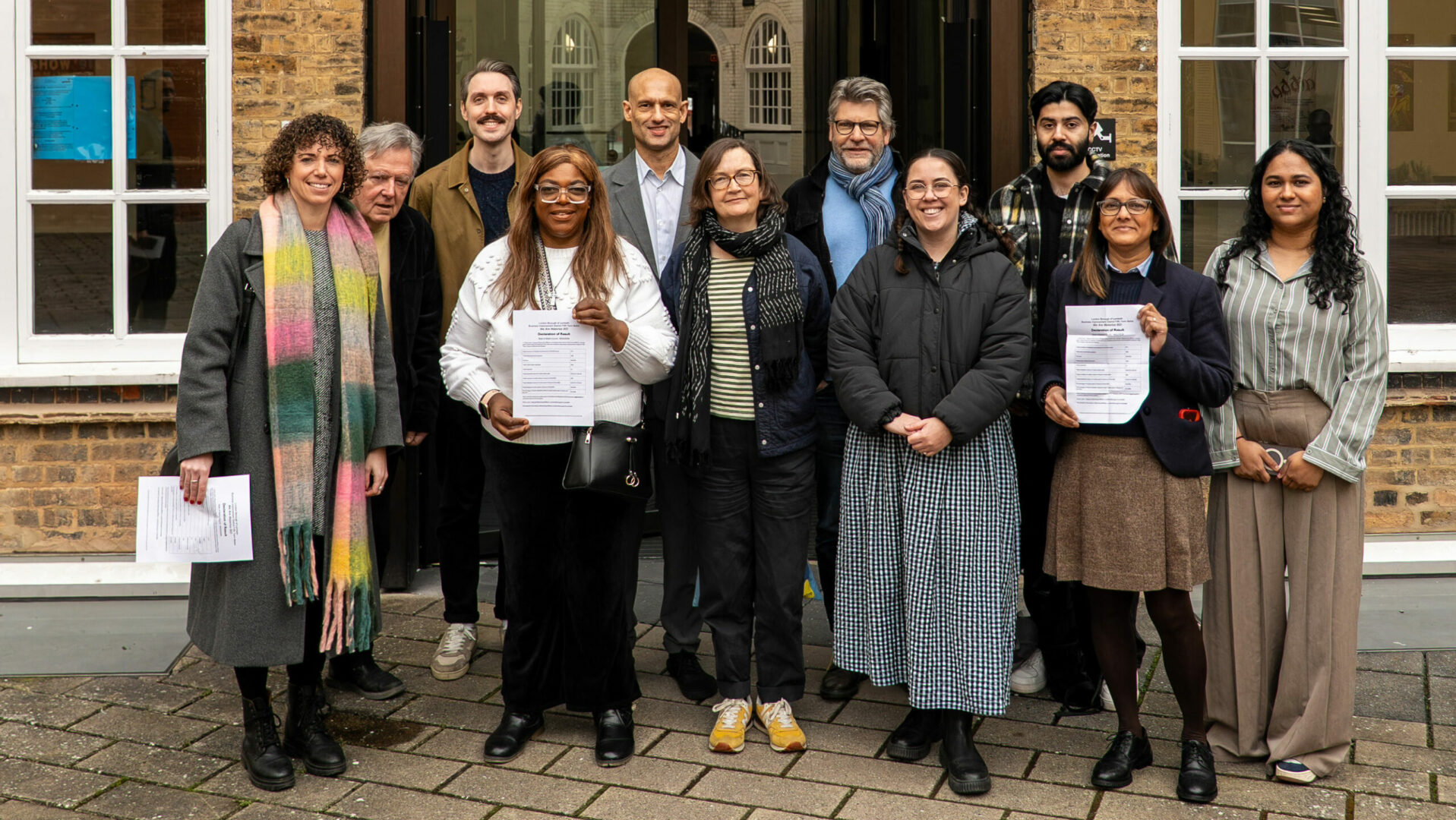 Members of We Are Waterloo BID, councillors and Lambeth officers standing outside Lambeth Town Hall courtyard, with two people holding printed documents.