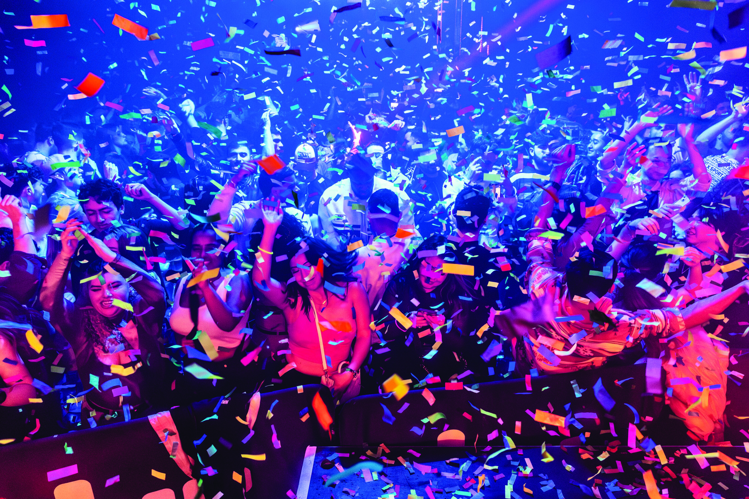 A nightclub room full of people smiling and dancing while confetti falls