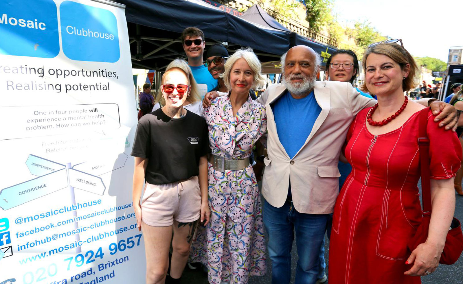 Brixton's MP and London's Deputy Mayor for Culture pose outdoors with community leaders and a poster for a local community organisation