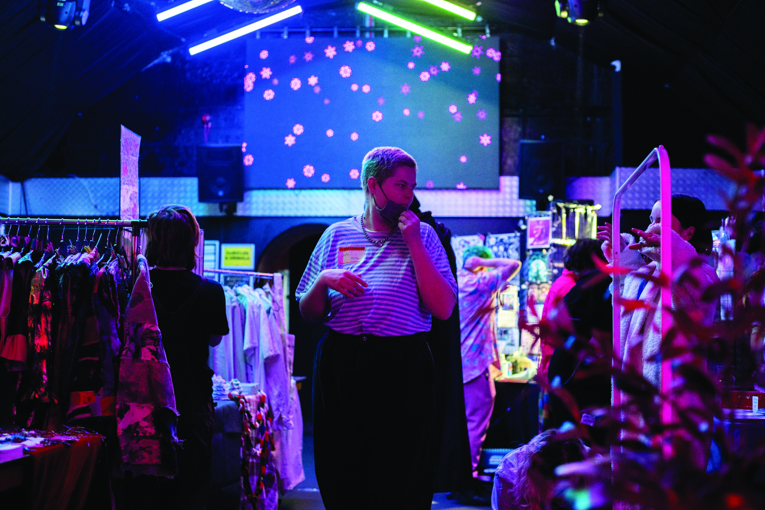 A small business owner walking between shop stalls set up in FIRE Nightclub as part of Queer Mart