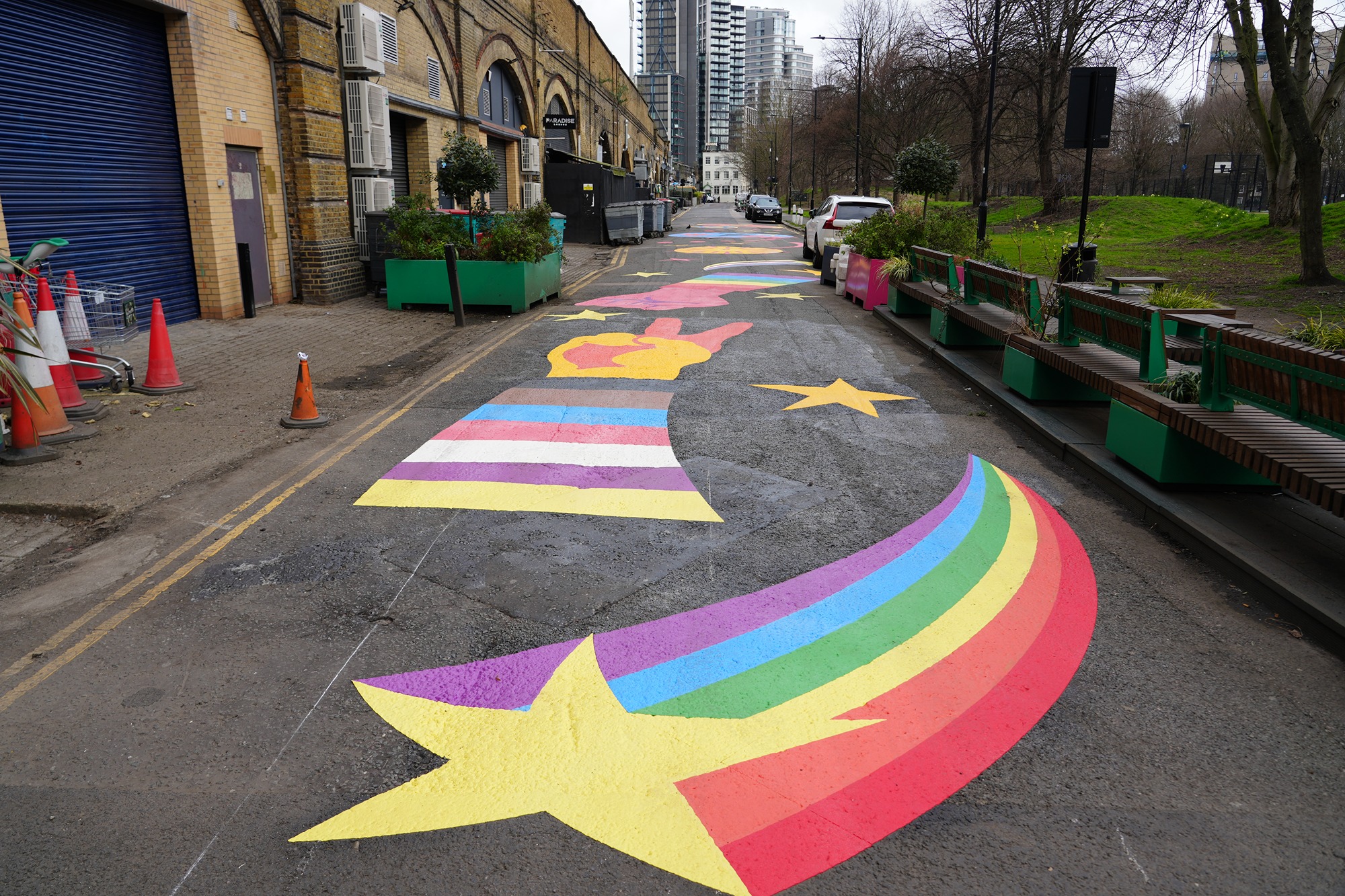 A mural on the carriageway showing a shooting star with a rainbow tail and an arm making a peace sign in the colours of the Progress Pride Flag