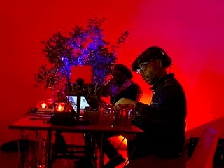 A sound artist performs seated in front of a light installation at Beaconsfield Gallery