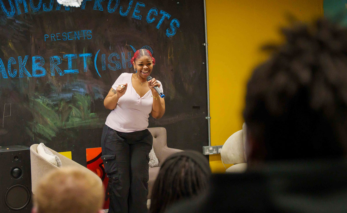 A young person speaking into a mic in front of a seated audience in a community space
