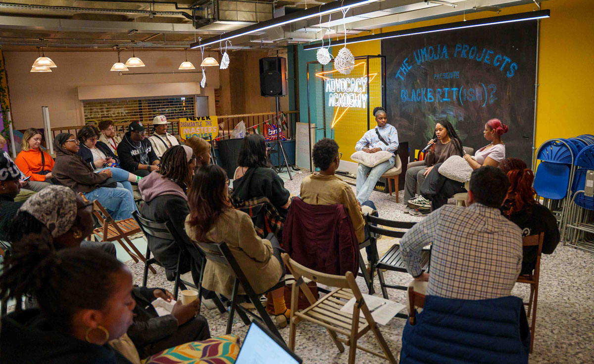 A seated audience of young people watching a panel of young people where one is speaking into a mic