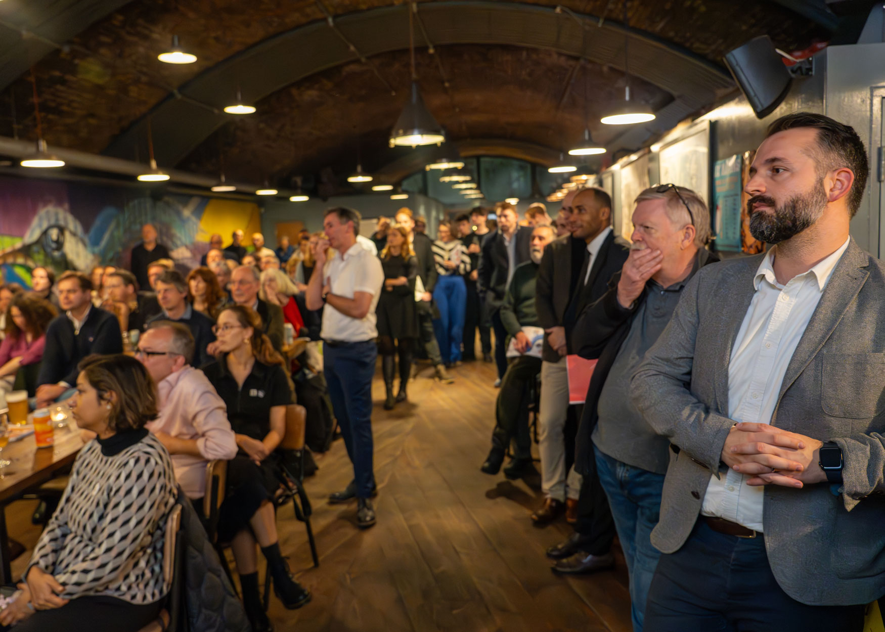 An audience of people standing and sitting in a bar and restaurant space