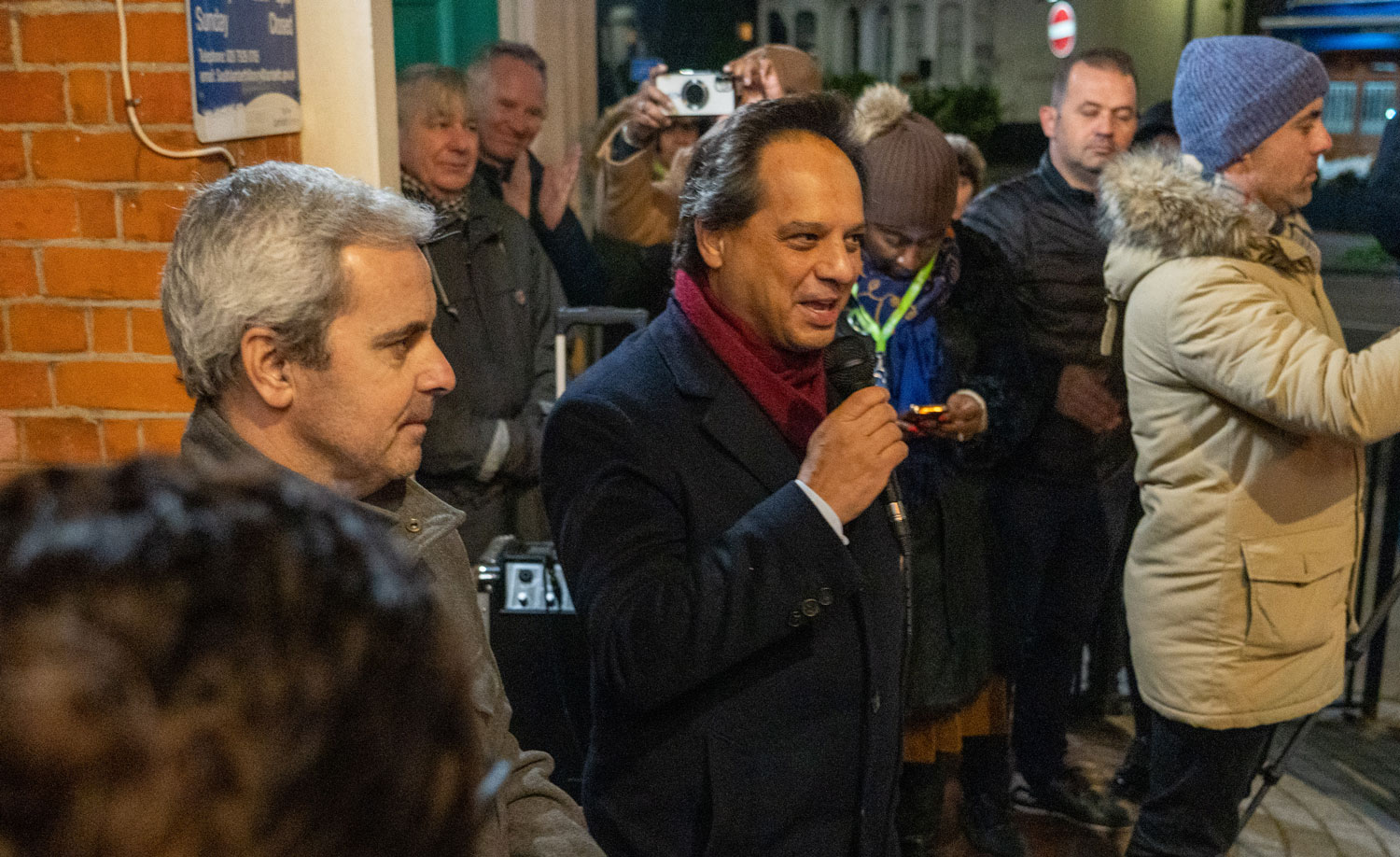 Officials from the Portuguese embassy speaking to a crowd of people standing outdoors at night