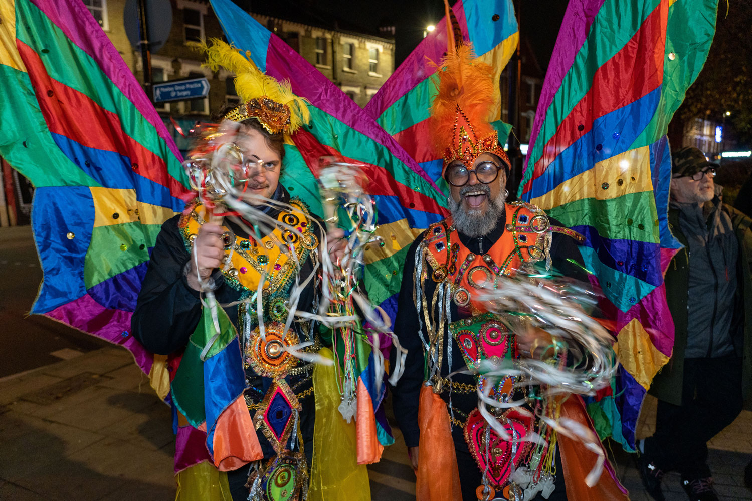 Two street performers dressed in colourful clothing and waving ribbons