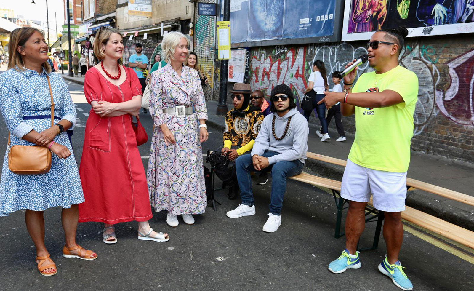 London's Deputy Mayor for Culture and Brixton community members watch a trumpet player performing outside in Brixton