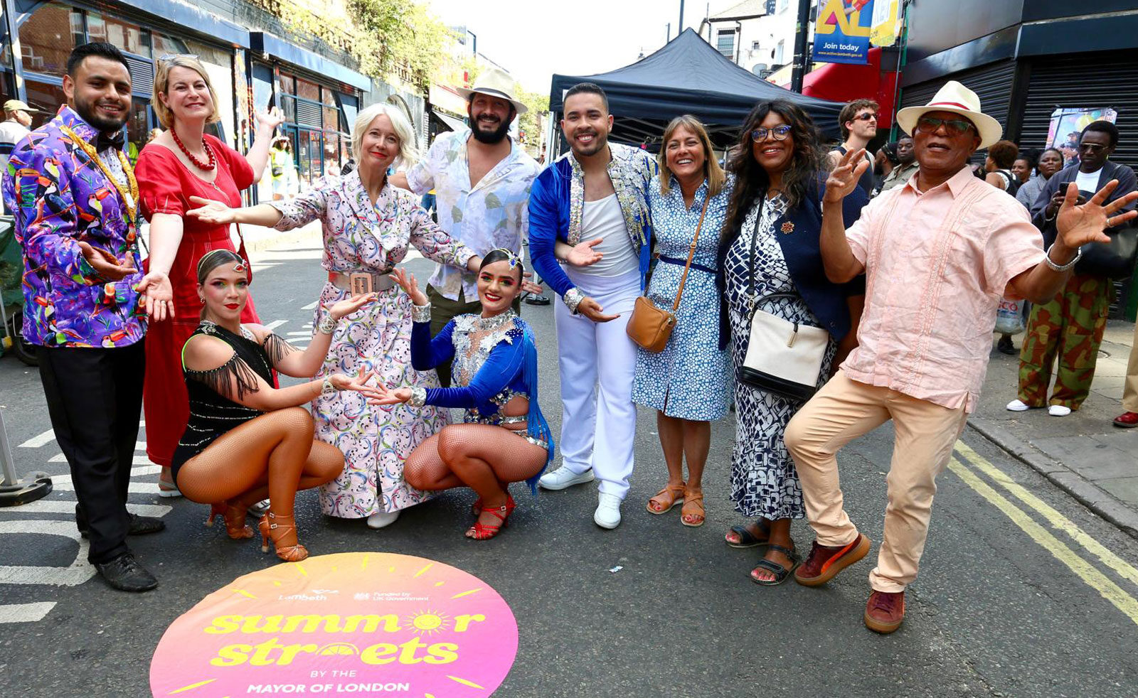 London's Deputy Mayor for Culture and Lambeth's Cabinet Members pose with dancers in costume on Atlantic Road in Brixton, in front of a road sticker reading "Mayor of London Summer Streets"