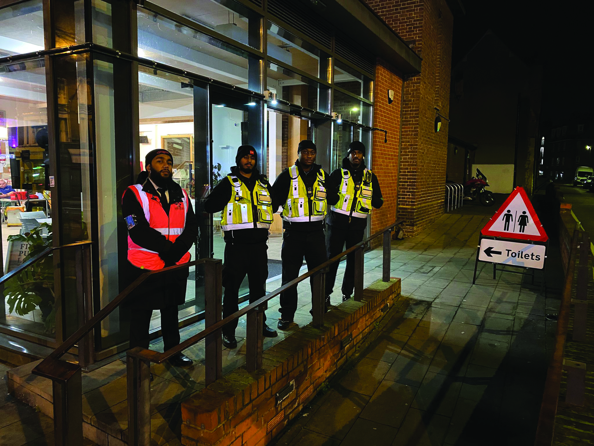 A group of five security workers in high visibility vests stand in front of the Clapham Night Hub ahead of their night time patrol