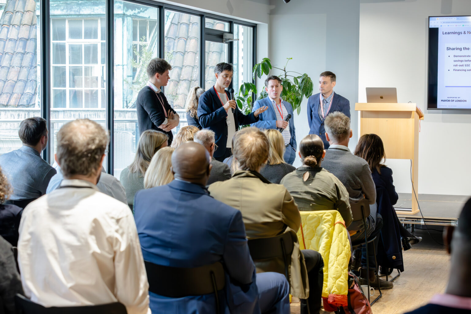 Four members of the innovation partnership team stand at the front of the stage speaking to a seated audience