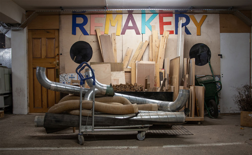 A workshop with wood and metal materials on a trolley. The wooden signage on the wall reads 'Remakery'