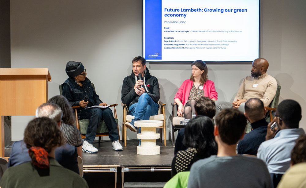 Four people sit on a stage during a panel discussion. The words on the screen behind them read 'Future Lambeth Growing Our Green Economy'
