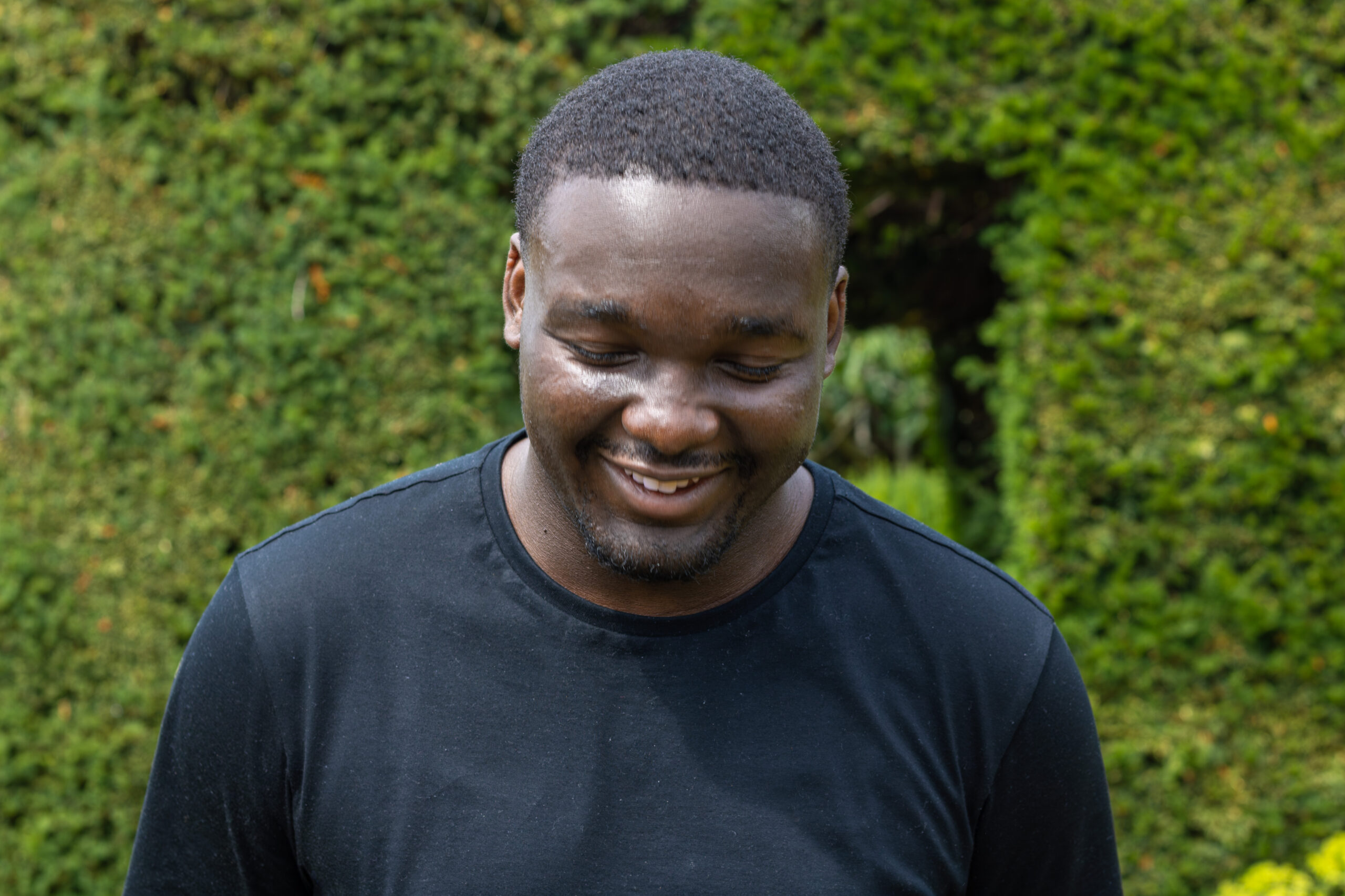Elevator wearing a black t-shirt, smiling in front of greenery
