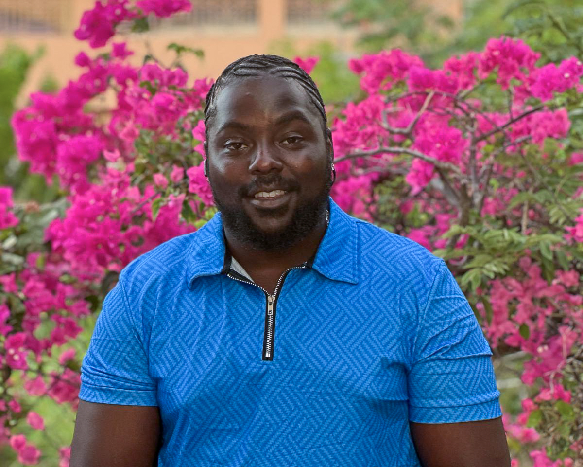 Elevator posing in blue shirt in front of pink flowers