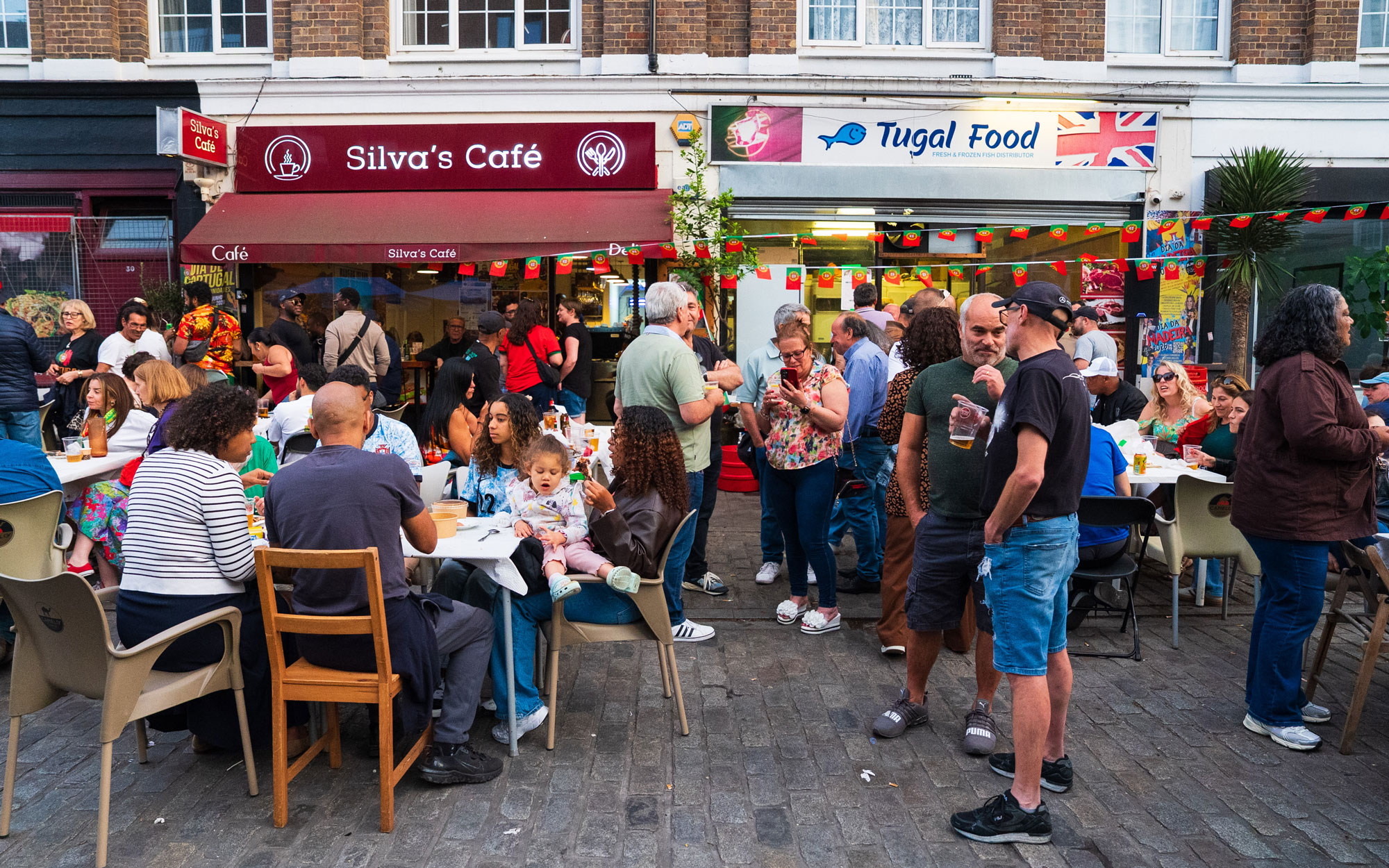 Families and visitors enjoy food and outdoor seating outside local cafés and businesses during Lambeth's Day of Portugal celebration.