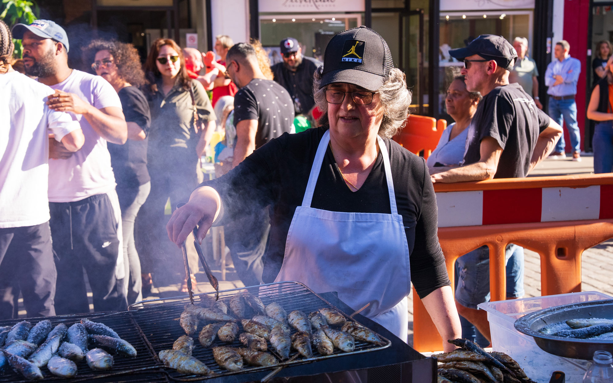 A volunteer grills fresh sardines at an outdoor barbecue as visitors gather for the Day of Portugal celebration in Little Portugal.