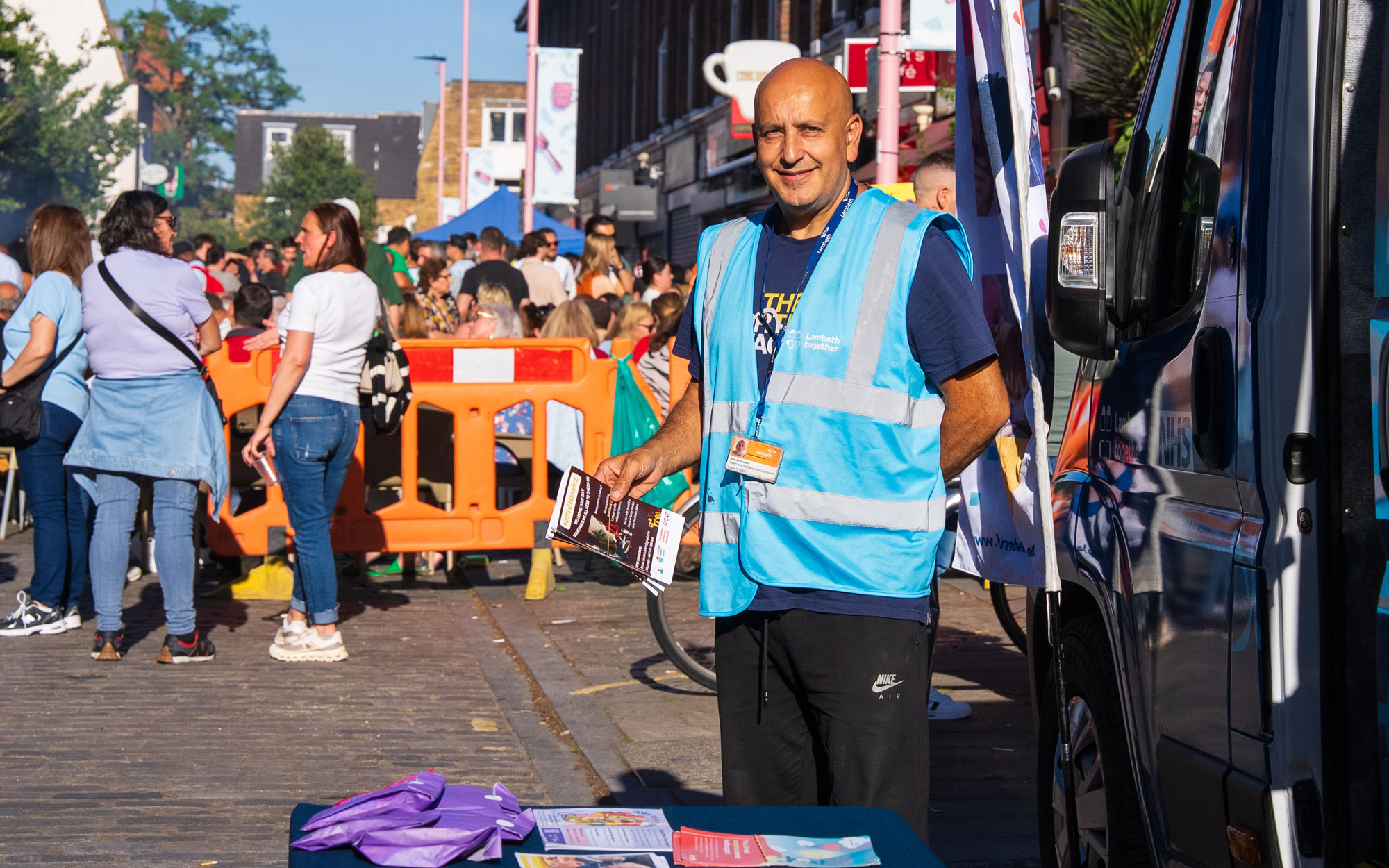Lambeth event volunteer in a blue high-visibility vest standing beside an information stall at the festival.