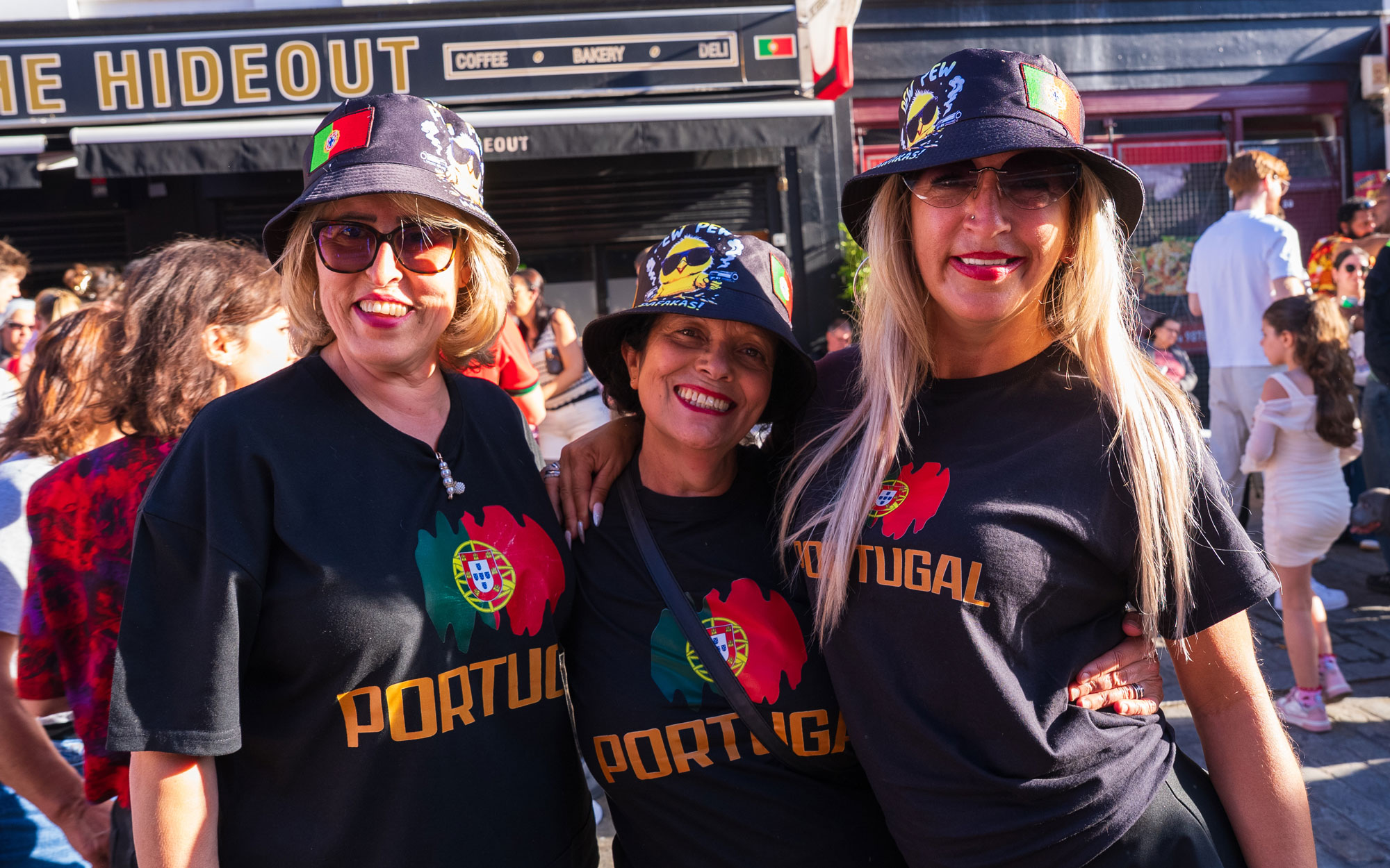 Three festival-goers wearing matching Portugal-themed clothing and hats pose together for a photograph.