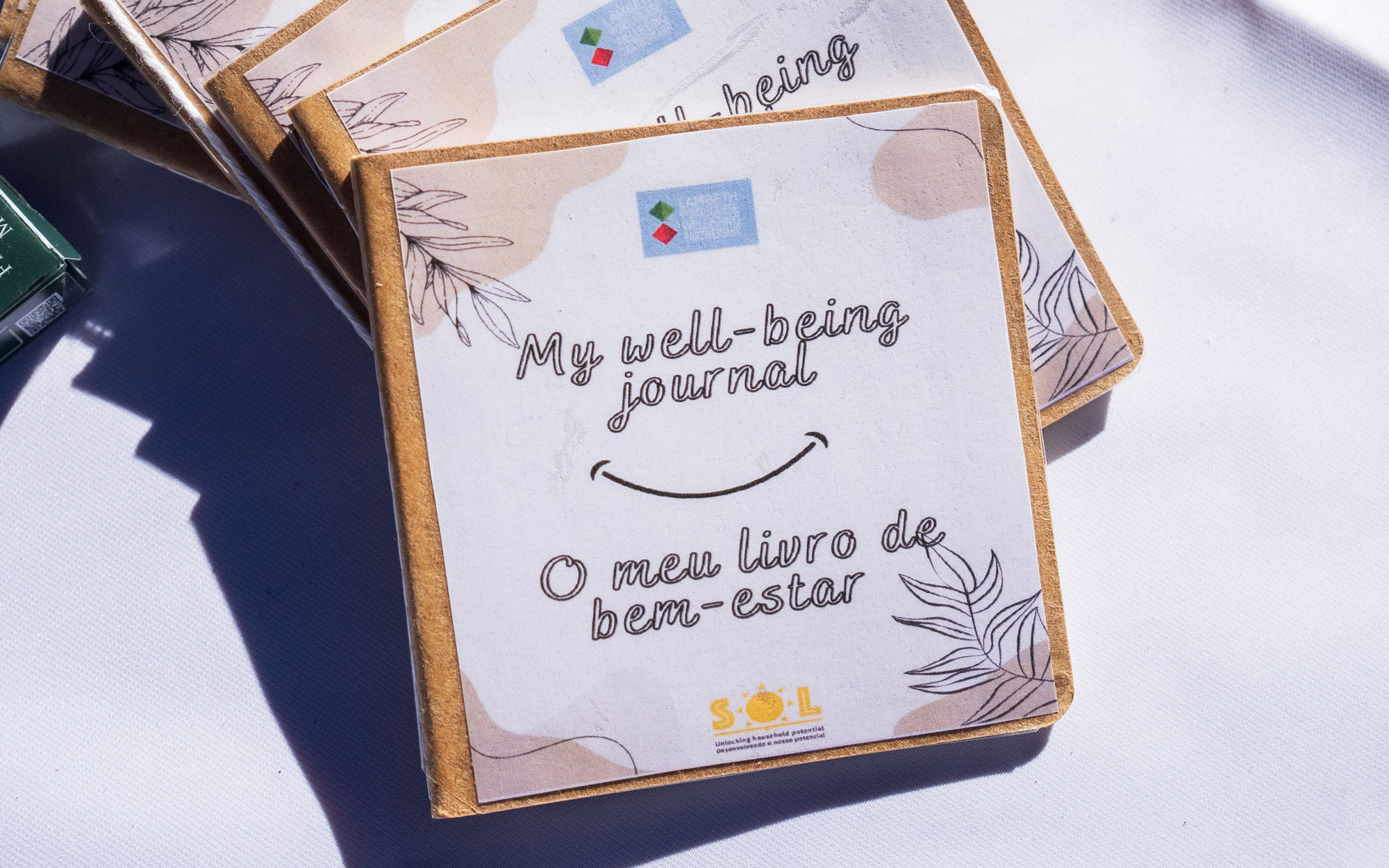 Stack of bilingual English and Portuguese wellbeing journals displayed on a table at a community sta