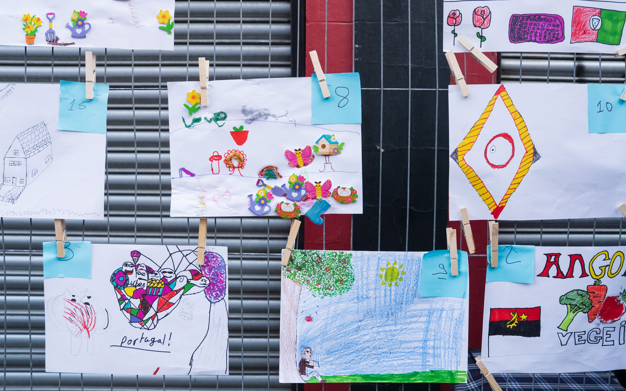 Children's drawings and colourful artwork displayed on a wire fence during the community festival.