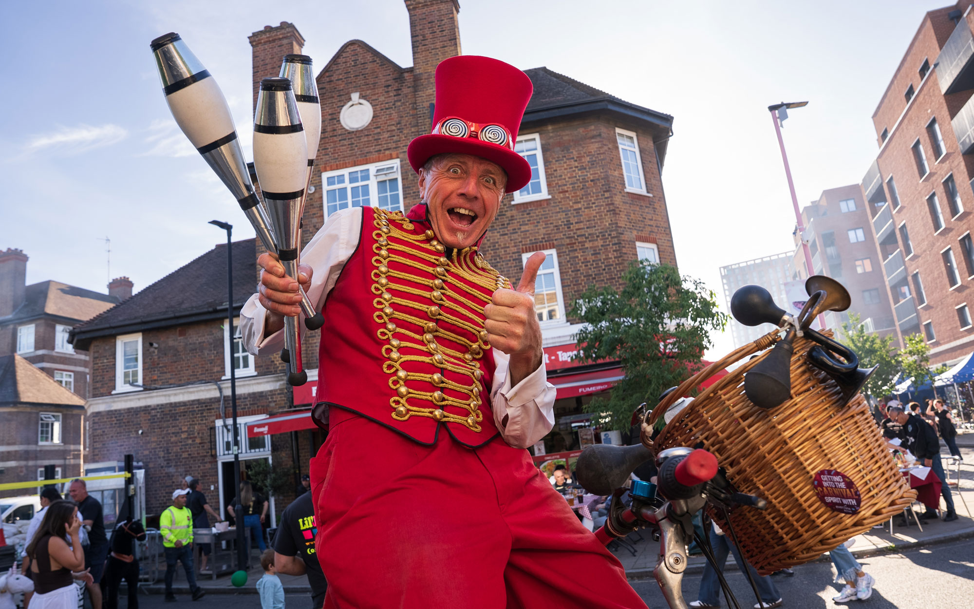 Street performer in a bright red costume and top hat juggles clubs while entertaining visitors at the Day of Portugal celebration in Little Portugal.