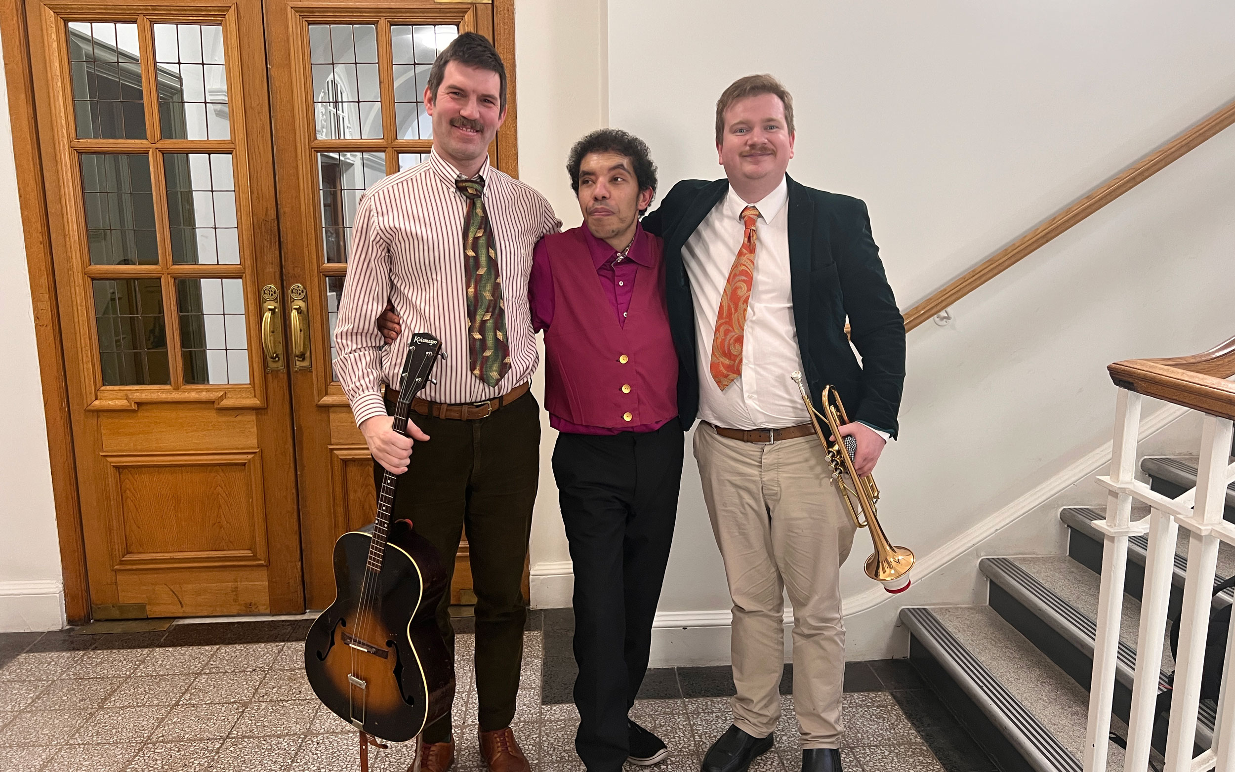 Three musicians pose together with a guitar and trumpet before performing at Danceology.