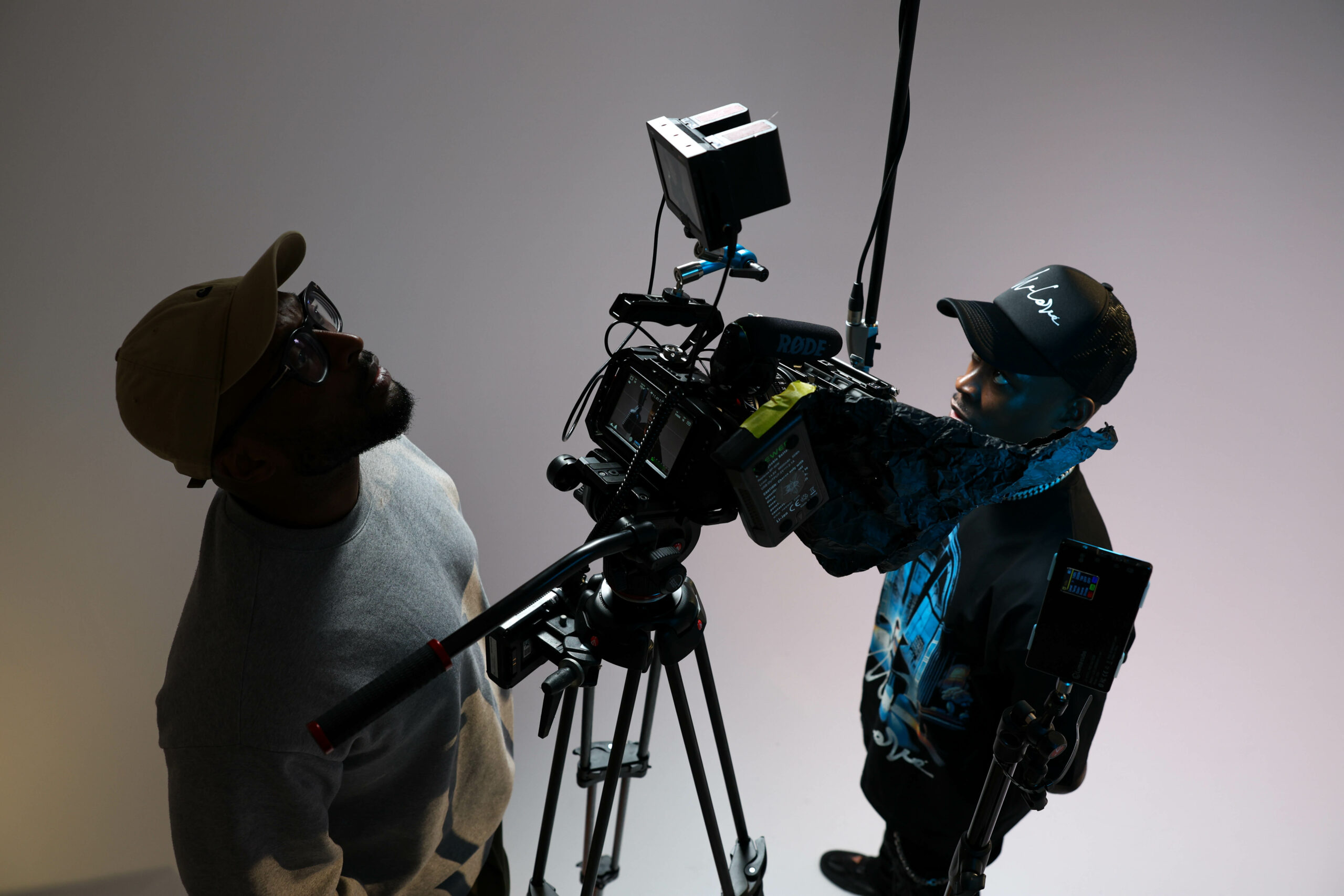 Two filmmakers adjust a professional video camera and lighting setup during a studio production.