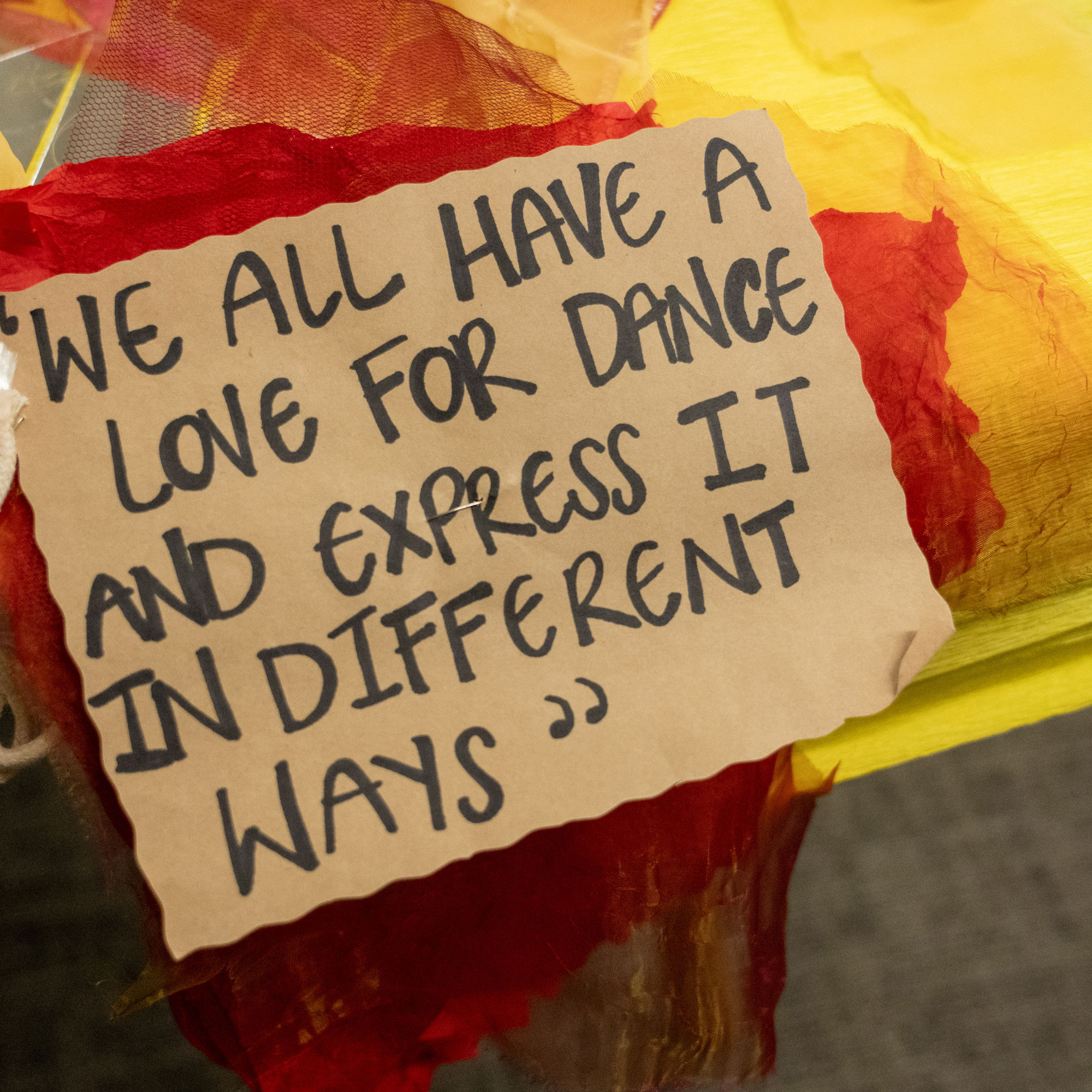 Handwritten quote reading, "We all have a love for dance and express it in different ways," displayed on colourful fabric.