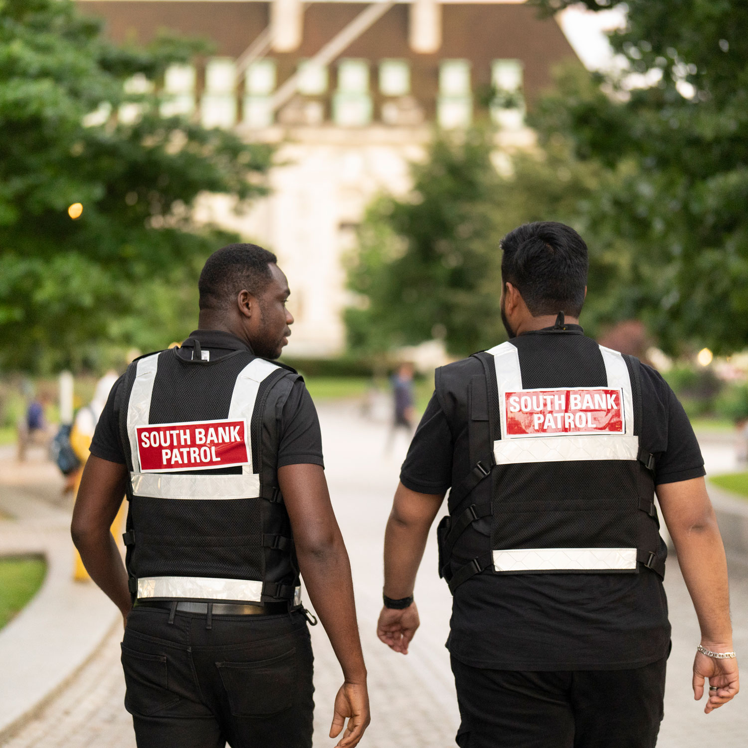 Two South Bank Patrol officers wearing high-visibility vests walk through a busy riverside park, providing a visible presence to help keep the area safe and welcoming.