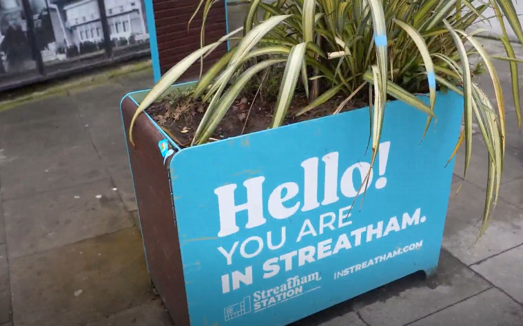 Blue planter outside Streatham Station displaying the message "Hello! You are in Streatham" with green plants growing from the top.