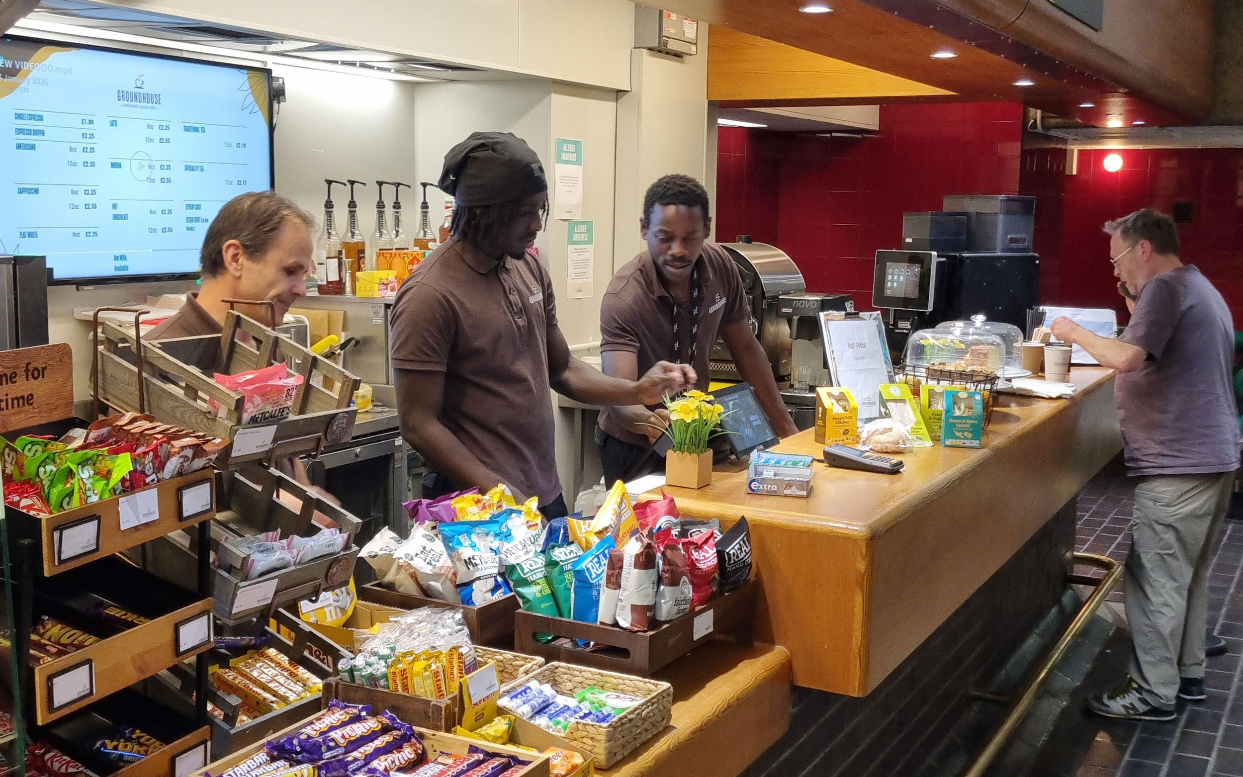 Mustafa and a colleague prepare drinks and serve customers behind the café counter.