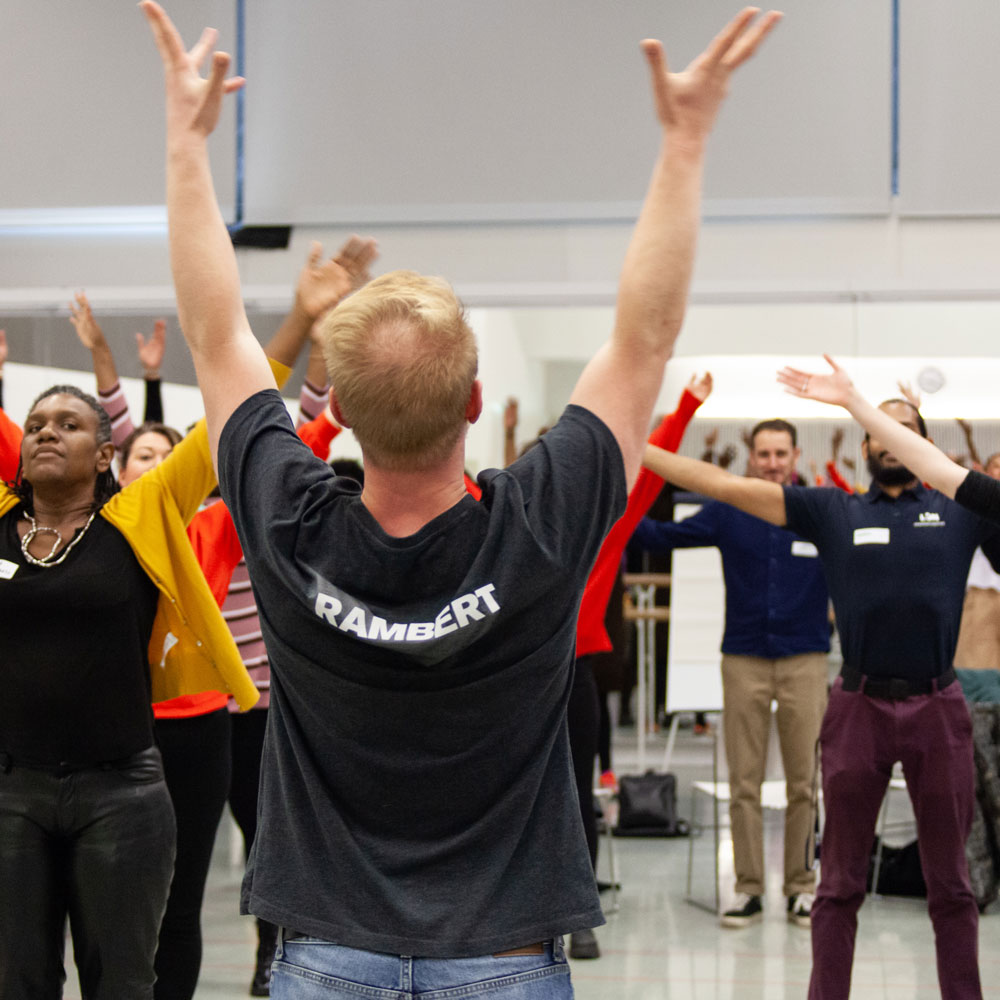 Participants raise their arms during a group movement workshop led by a Rambert facilitator.