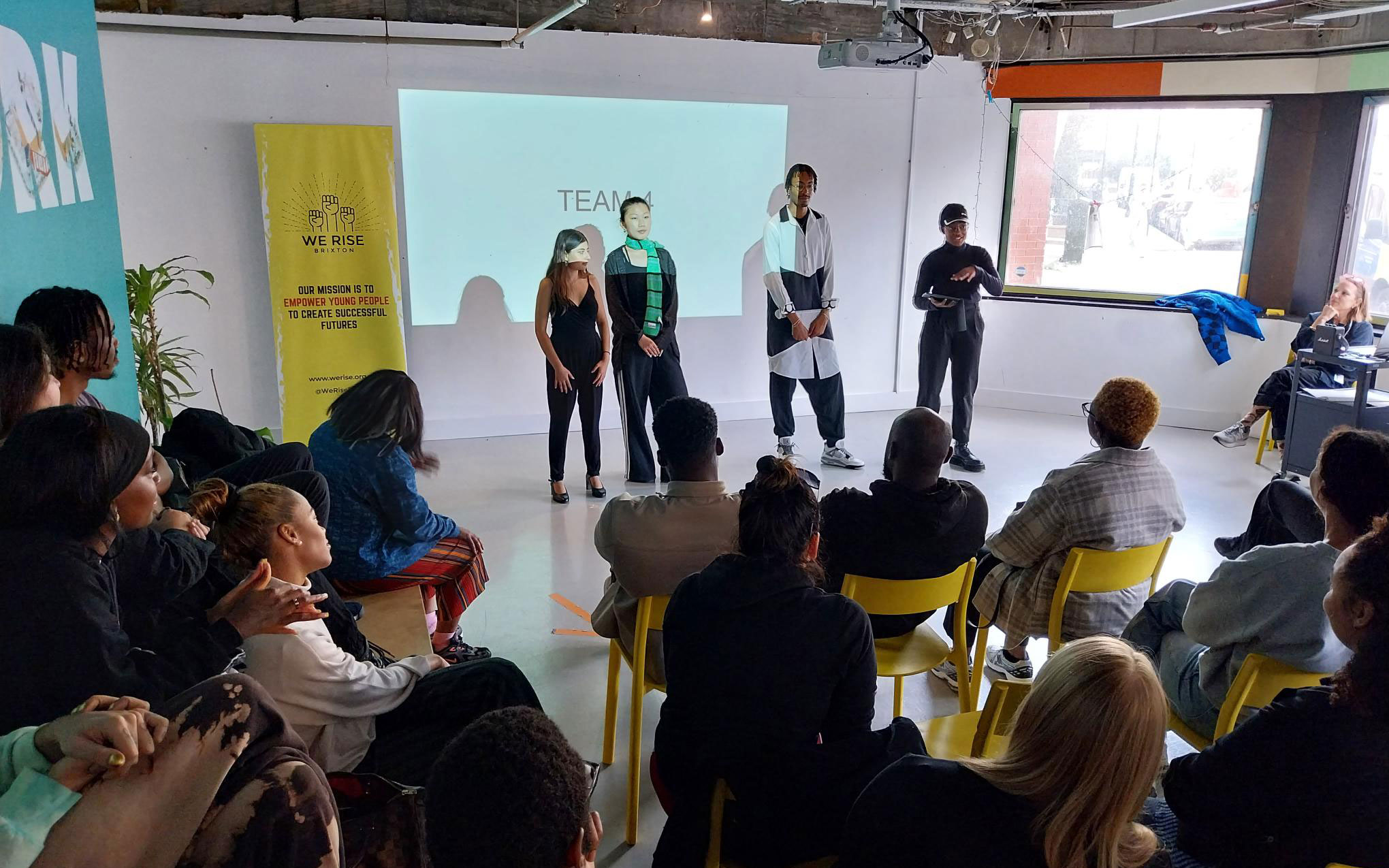 Young people deliver a team presentation to an audience at a We Rise Brixton bootcamp