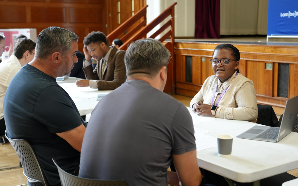 A Project SEARCH candidate speaks with two employers during an interview, seated around a table at an event in Lambeth.